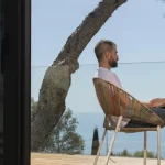 Man working on a laptop on a balcony on sunny seafront