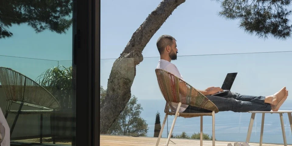 Man working on a laptop on a balcony on sunny seafront