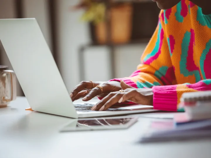 Hands typing on a laptop beside colourful fabric