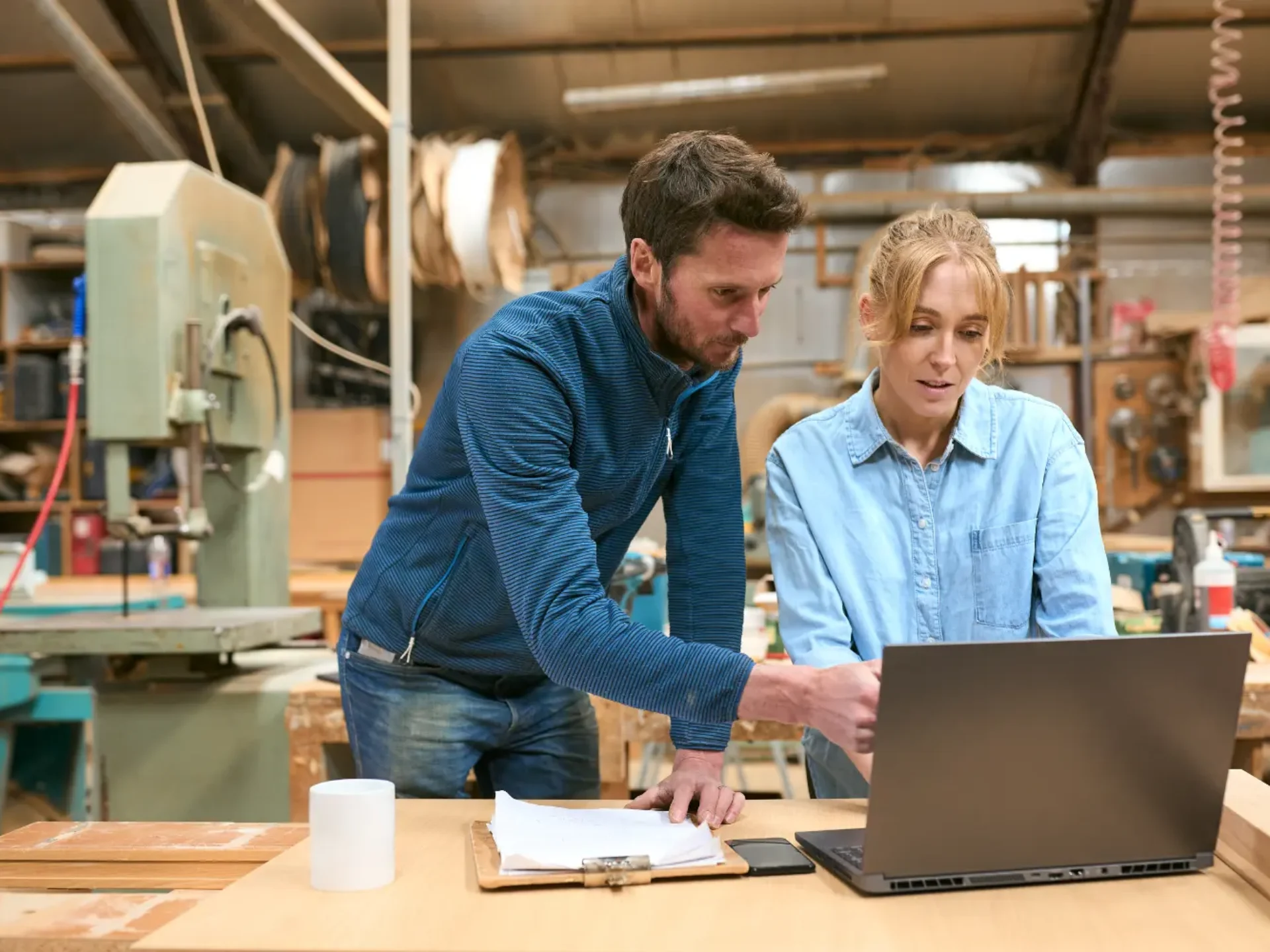 Man and woman reviewing figures on a laptop in a workshop.