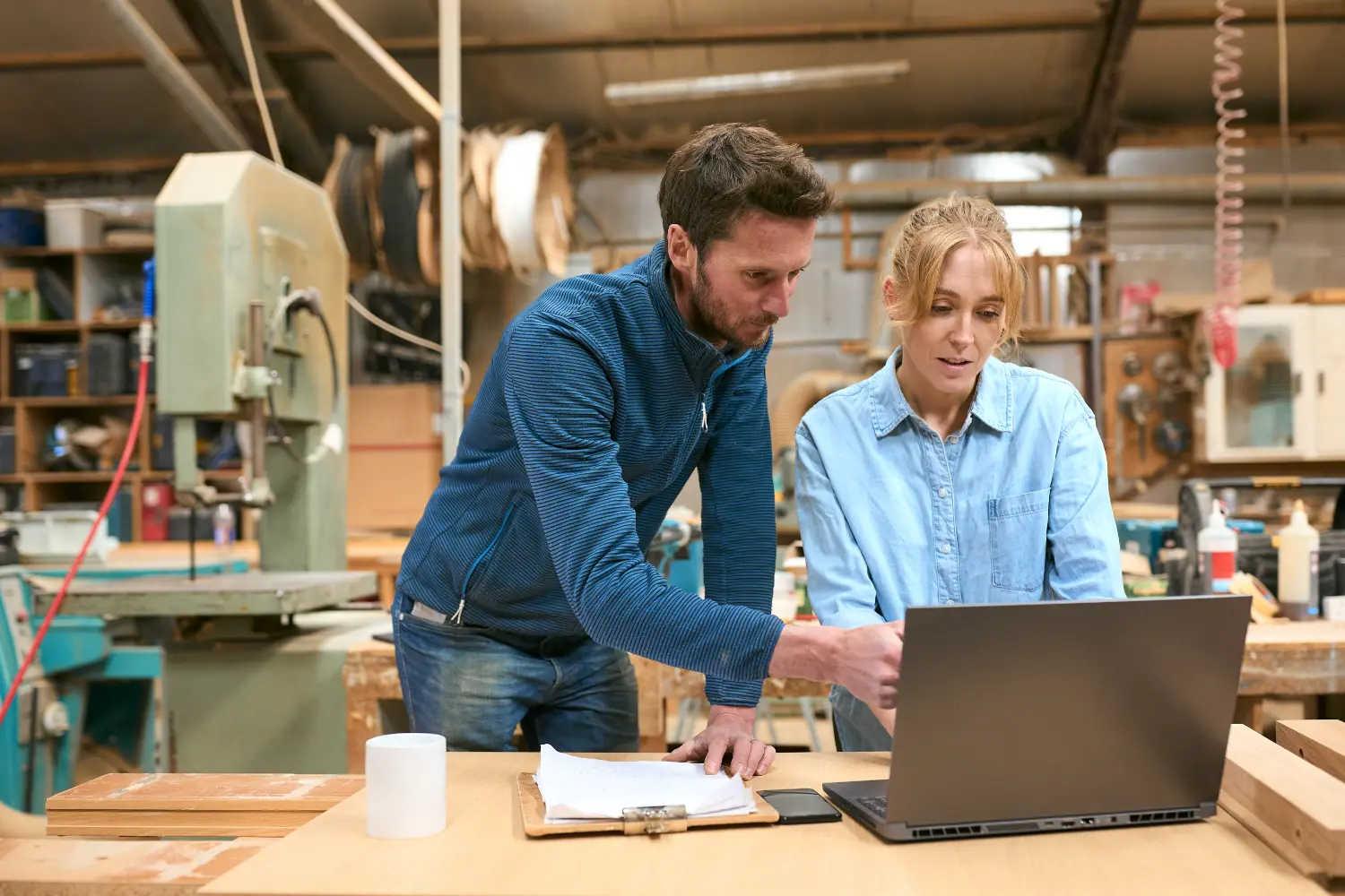 Man and woman reviewing figures on a laptop in a workshop.