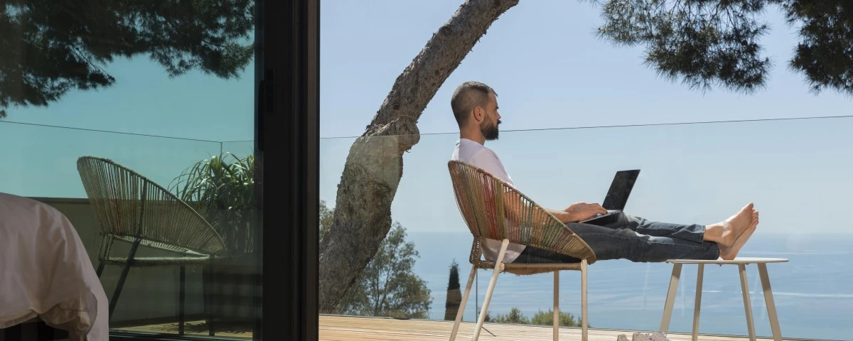 Man working on a laptop on a balcony on sunny seafront