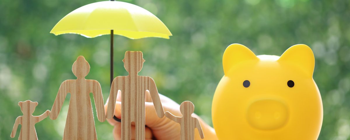 Piggy bank and wooden family figurines shielded by umbrella