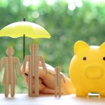 Piggy bank and wooden family figurines shielded by umbrella