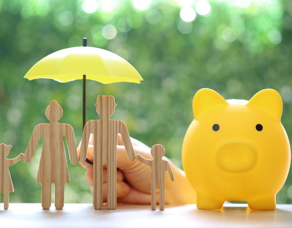 Piggy bank and wooden family figurines shielded by umbrella